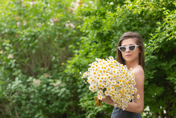 Young girl in glasses with a bouquet of daisies on the street