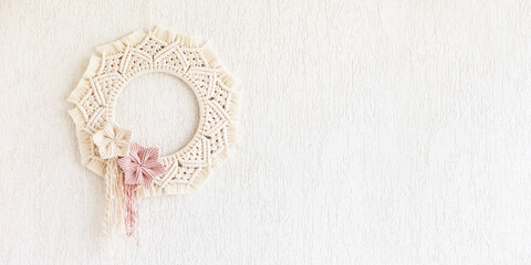 Macrame wreath with cotton flowers on a white decorative plaster wall. Natural cotton thread and...