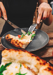 woman hands with knife and fork cutting neapolitan pizza on table in cafe outdoor