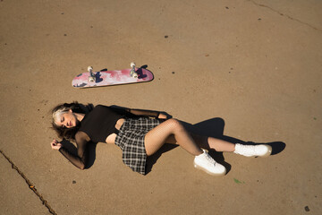 Young and pretty girl with punk style lying on the ground with her skateboard next to her.