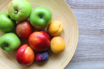 Wooden bowl with various colorful fruit on dark background. Top view.