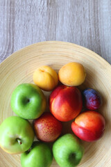 Wooden bowl with various colorful fruit on dark background. Top view.