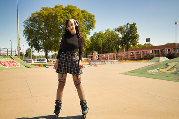Pretty young girl with pigtails, white headphones and punk style inline skates skating with gay...