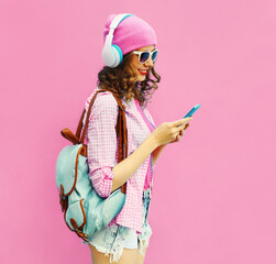 Summer colorful portrait of stylish modern young woman listening to music in headphones with smartphone on pink background