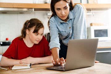 White woman helping her daughter with down syndrome using laptop