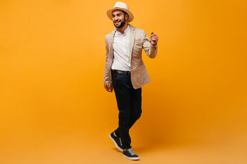 Fototapeta na wymiar Cool man in suit and cap walking on orange studio