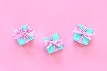 Three green present boxes with bow on pink background. Top view, flat lay