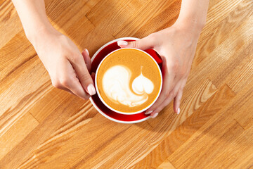Hands hold a cup of cappuccino. Drawing in a cup.