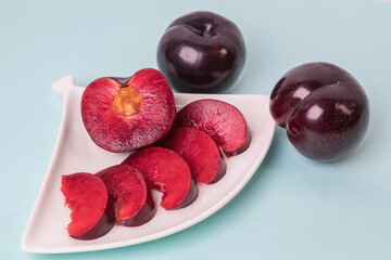 On a white saucer there is a large plum cut into wedges, next to it there are two more plums. The...