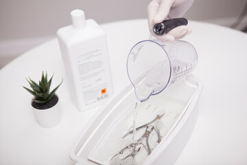 Close up of manicurist pouring liquid sterilizer into container with nail nippers