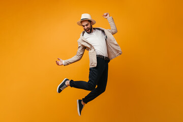 Fototapeta na wymiar Man in hat and beige jacket jumping on orange background