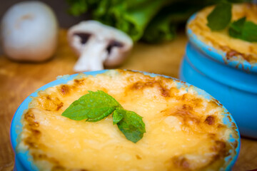 A pot of mushroom julienne on a wooden board, decorated with herbs. Julienne in cocotte with yellow cheese crust. Close-up.