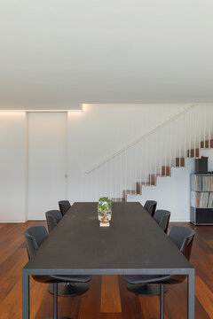 Frontal View Of Modern Dark Table With Chair. In Background There Are Cantilever Staircase And Library. Luxury Wooden Floor. Interior Of Design Apartment