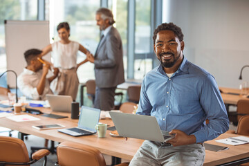Mature black businessman with colleagues sitting in a modern board room. Proud smiling business man sitting during a meeting and looking at camera. Portrait of happy successful executive with team 