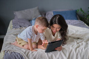 mother and son with tablet at home. Mother showing media content on line to her son in a tablet in the living room in a house interior