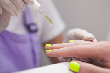 Close up of unrecognizable manicurist applying cuticle oil on clients hands after manicure