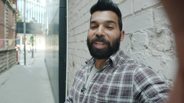 POV portrait of handsome young Arab man speaking and waving hand looking at camera making video call in the street smiling enjoying conversation
