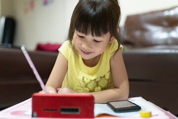 Fototapeta na wymiar Cute Asian girl using smartphone to study online with teacher on video call at home. homeschooling, distance learning. quarantine concept. online education.
