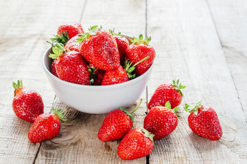 Red juicy strawberries in a bowl on wooden table with copy space, summer fruits containing...