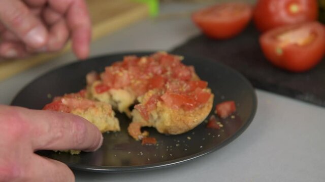 a male hand taking un piece of frisella of plate, dry bread with tomato, oregano and olive oil is a tipical summer dish of Puglia. Healthy vegetarian food, close up
