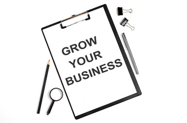 On a white background magnifier, a pen and a sheet of paper with the text GROW YOUR BUSINESS . Business concept