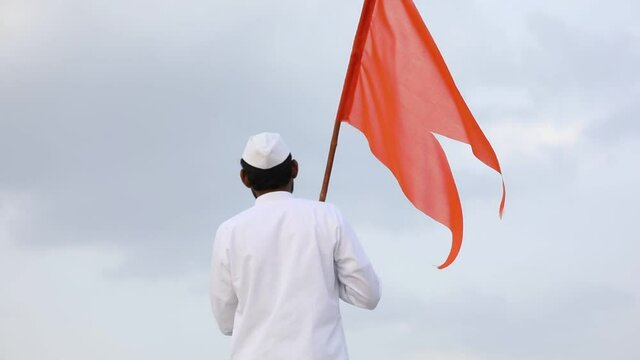 Young indian man (pilgrim) in traditional wear and waving religious flag.