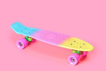 Pastel neon rainbow colored Penny board skateboard isolated on solid soft pink background. Plastic mini cruiser. Youth minimalistic Sport inspired summer fun concept. Copy space.