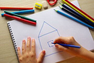 A child draws a house in an album , a pencil in his hands, a notebook, an eraser