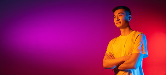 Flyer. Asian young man isolated on studio background in gradient pink purple neon light, colour...
