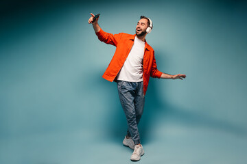 Man in stylish outfit dancing on blue background and holding smartphone