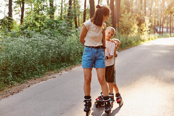 Mother with sons spending time together in summer park, family rollerblading, active pastime,...
