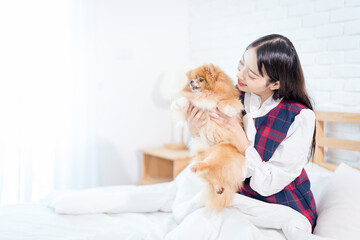 Asian girl holding a Pomeranian on a white bed. Young pretty woman hold in hands small Pomeranian dog.