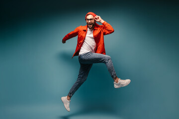 Fototapeta na wymiar Man in bright outfit holds glasses and jumps on blue background