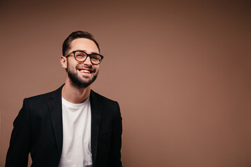 Joyful man in white T-shirt and jacket smiling on brown background