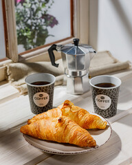 breakfast with two croissants and two paper cups of coffee