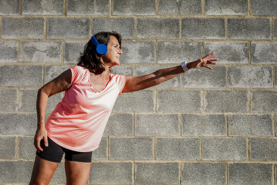 Hispanic Woman 60 Years Old With Sportswear And Headphones Stretching Arm