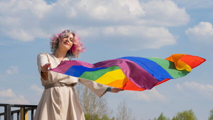 Caucasian woman with curly colored hair holding lgbt flag. Lesbian woman holding a rainbow flag outdoors