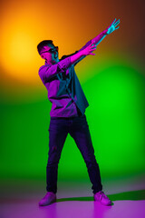 Young man, fashion model in casual clothes isolated on studio background in gradient green yellow neon light, colour filter. Concept of human emotions, facial expression.