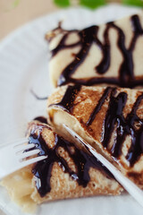 Pancakes drizzled with chocolate on a plate in a restaurant. Breakfast at the cafe. A woman eats pancakes for breakfast from disposable dishes. Top view and vertical photo