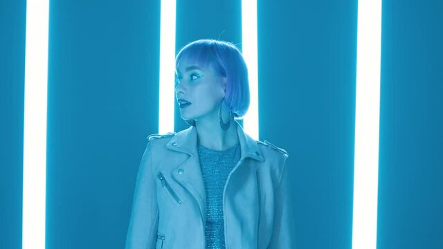 Charismatic woman with pink hairstyle posing near led-blue glowing neon lamps. Hipster trendy girl. Modern model pop outfit, influencer lifestyle. Slow motion.