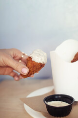 Close-up of chicken wings fried in batter. In a fast food restaurant, there is a cardboard box of chicken and sauce on the table. Sun rays fall beautifully on the hand of the girl who holds the food
