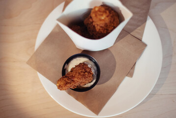 Close-up of chicken wings fried in batter. In a fast food restaurant, there is a cardboard box of chicken and sauce on the table. Sun rays fall beautifully on the hand of the girl who holds the food