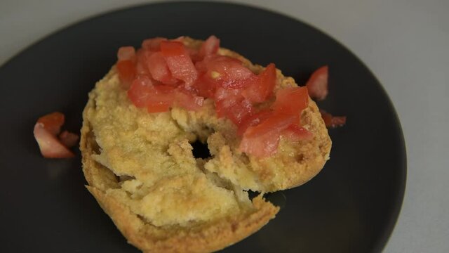 A man prepare a friselle, typical dish of Puglia: dry bread with tomatoes, oregano and olive oil: putting a cutting tomatoes on the frisa. Healthy vegetarian vegan food, close up