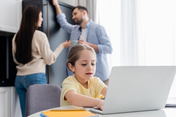 blurred couple talking near child typing on laptop while doing homework