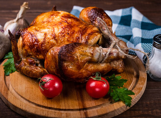 Whole fried chicken with a golden crust. Wooden background. Vegetables, garlic and tomatoes.