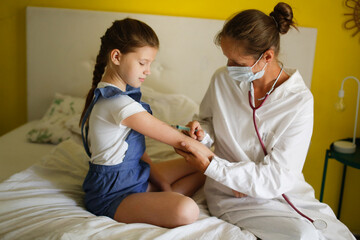 nurse in mask and white coat injects child girl with syringe, calling doctor at home, patronage. Treatment of pediatrician at home in real interior, concept of medicine and disease prevention