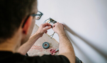 Unrecognizable male electrician wrapping cable with electrical tape on the electrical installation...