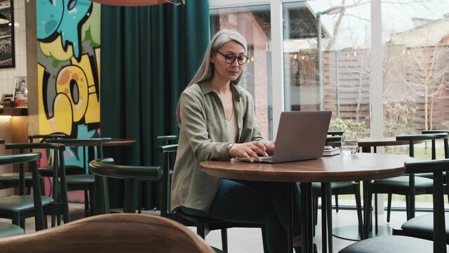 A serious woman wearing eyeglasses using her laptop sitting at the cafe inside