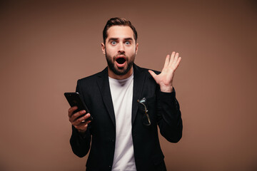 Blue-eyed guy in suit stares in astonishment at camera and holds phone