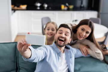 Fototapeta premium selective focus of cellphone in hand of excited man taking selfie with happy family